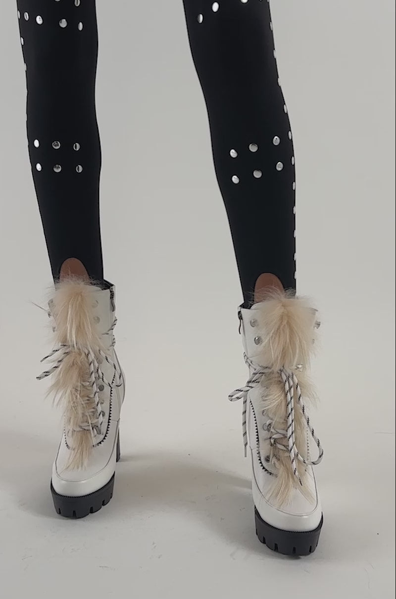 Video of a woman modeling the AKIRA GOLD SNUG WHITE FUR BLOCK HEEL COMBAT BOOTIE, showcasing the cozy elegance of this stylish white lace-up bootie with fur trim and a modern chunky lug sole.