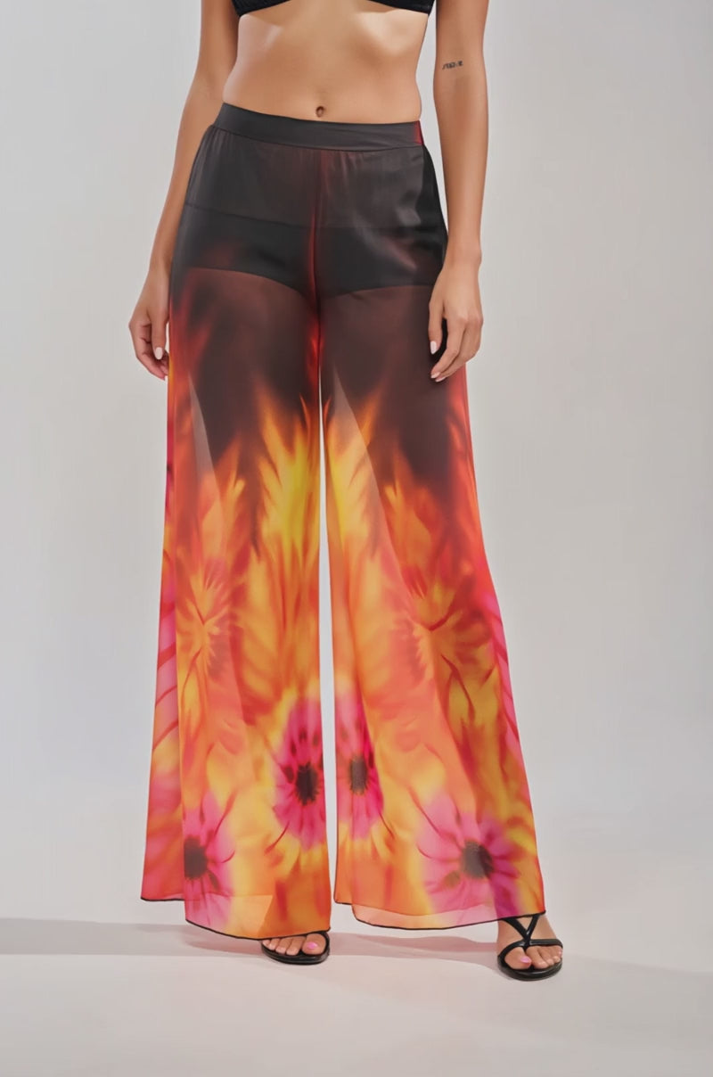 Video of woman modeling the GIRL ON FIRE CHIFFON PALAZZO PANT—sheer, high-waisted, wide-leg floral pants in vibrant orange, yellow, and pink—with black sandals for a chic look.