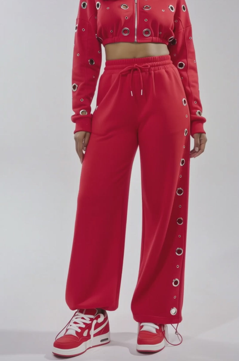 A video of a woman in the COMFY COZY CROPPED HOODIE and matching red sweatpants with grommet details, paired with red and white sneakers, set against a plain light background.
