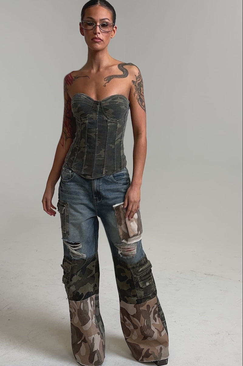 Video of woman modeling the MIXED CAMO DENIM CARGO PANTS with a wide-leg silhouette, camo patchwork on the thighs and lower legs, distressed details, and large cargo pockets, stylishly paired with open-toed heels.