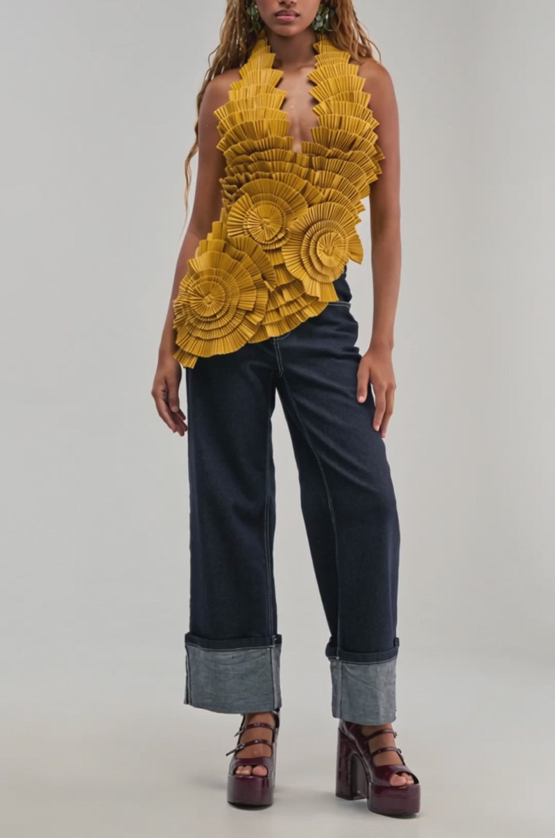 Video of a woman modeling MOLTEN PETAL PLEATED TOP—a sleeveless, yellow sculptural blouse featuring large, pleated, fan-like ruffles.