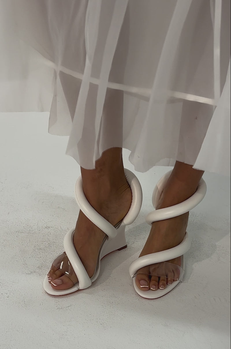 Video of woman modeling the AKIRA MINORU WHITE WEDGE SANDAL with clear and white straps and a sheer white skirt.