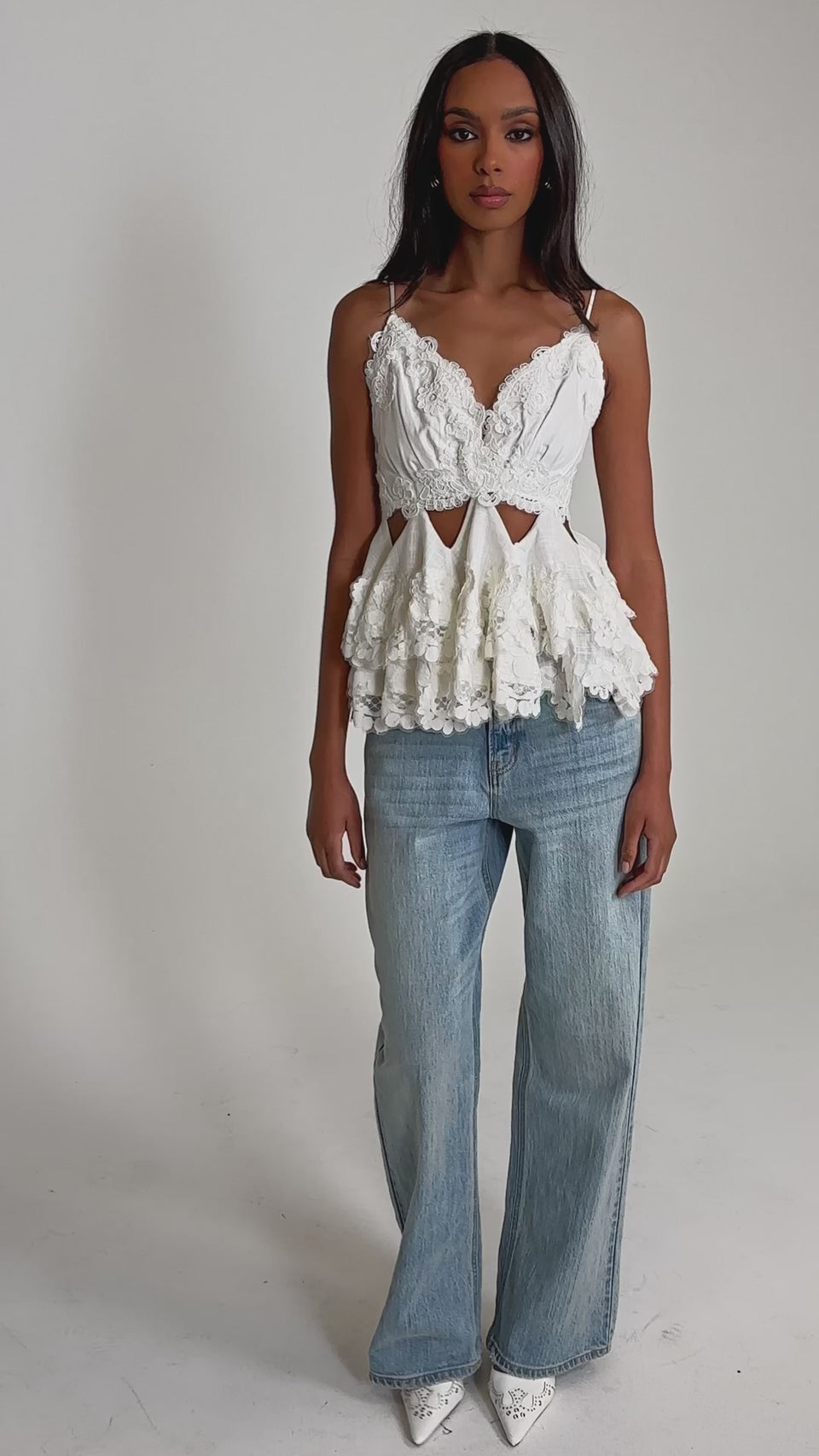Video of woman modeling the LOTS OF LOVE TO GIVE TO YOU LACE BLOUSE, featuring white floral lace, ruffled sleeves, and cut-out details, paired with light blue jeans. 