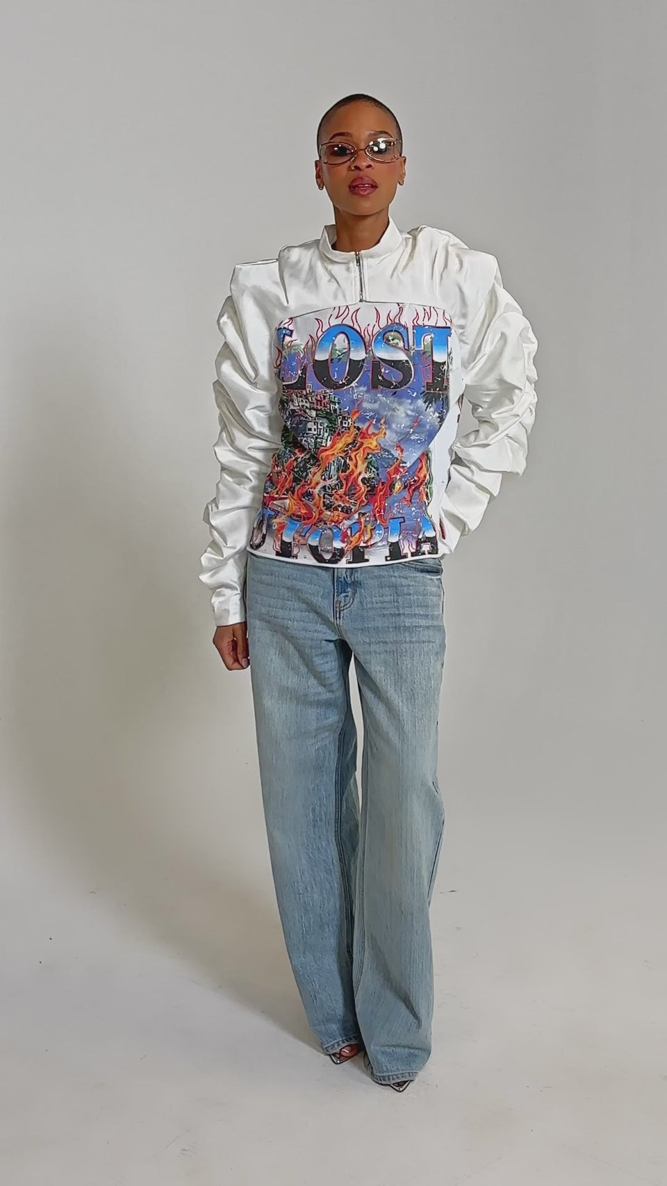 Video of woman modeling the CORA SATIN BOLERO IN WHITE featuring ruched sleeves and a vibrant "LOST UTOPIA" graphic of flames and city imagery.