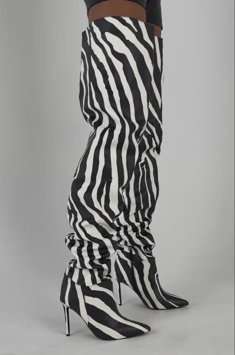 Video of a woman modeling the AZALEA WANG BOMBSHELL ZEBRA THIGH HIGH BOOT—bold statement footwear—while holding a small handbag.