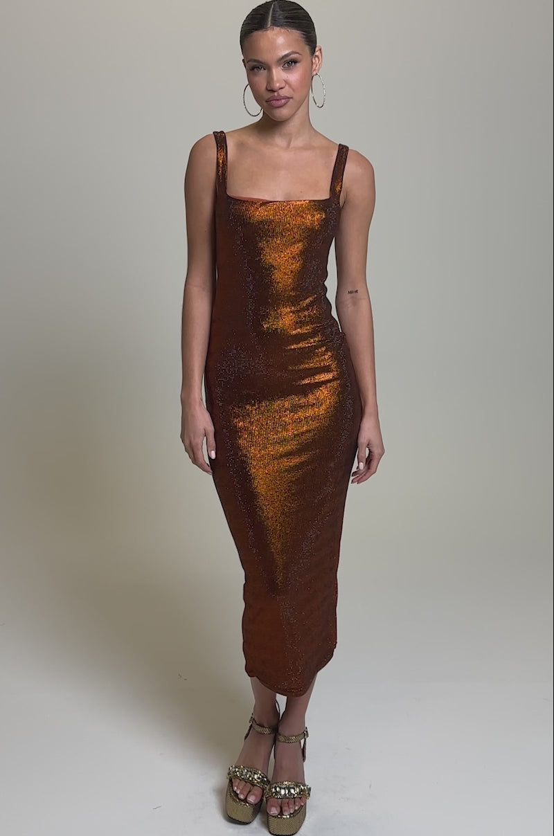 Video of woman modeling the AKIRA Label CLASSY BUT SASSY RHINESTONE MIDI DRESS IN RUST, a fitted, shimmering rust dress with wide straps and a square neckline. She accessorizes with platform heels and hoop earrings against a plain light gray background.