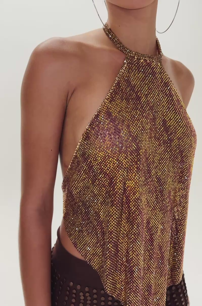 Video of woman modeling the GOLDEN GLAM RHINESTONE TOP—a metallic halter with a pointed hem—paired with brown high-waisted shorts with gold studs. She wears slicked-back hair, large hoops, and has a neutral expression