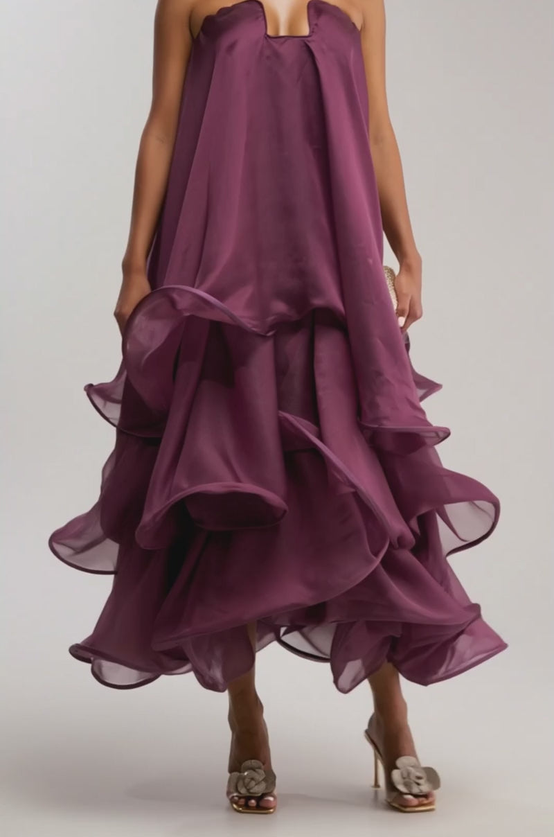 Video of woman modeling the BUDDING ROMANCE ABSTRACT MAXI DRESS IN PURPLE, featuring a strapless, layered ruffled design. She accessorizes with statement earrings and open-toe heels, creating a chic look for formal occasions against a light backdrop.