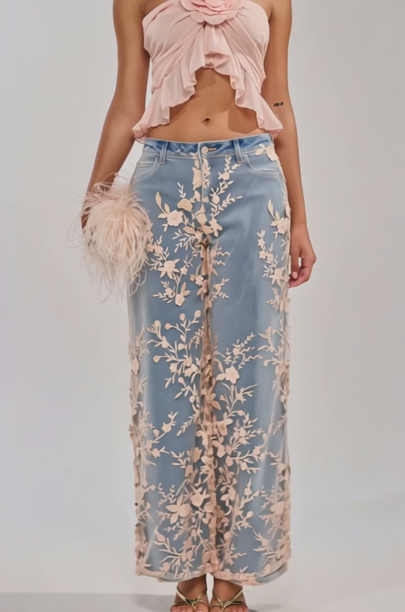 Video of woman modeling the FLY AWAY WITH ME TOP IN PINK—a cropped chiffon halter with ruffles and a large floral accent—paired with embroidered blue jeans, a beige feathered clutch, and gold hoop earrings.