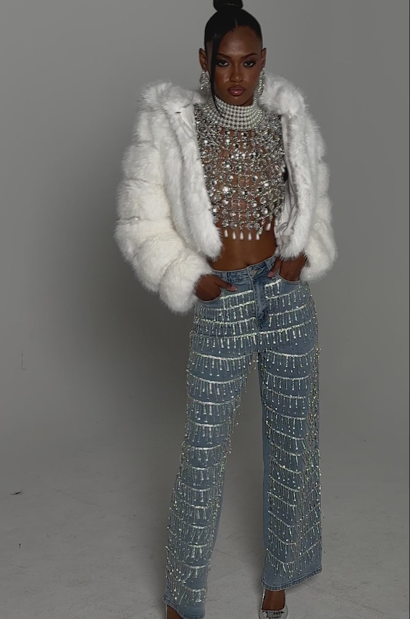 Video of woman modeling the DRIP DRIP EMBELLISHED DENIM high-rise wide-leg jeans with sparkling silver beads, a white furry jacket, and pointed silver high heels.