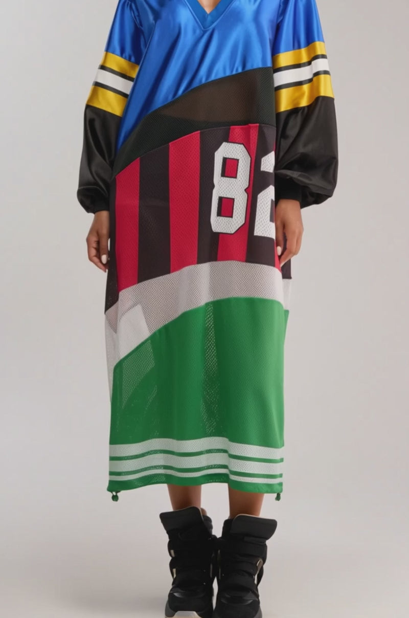 A video of a woman wearing the RARE GEM JERSEY MAXI DRESS—a colorblocked blue, black, red, and green dress with "82"—paired with black high-top sneakers.