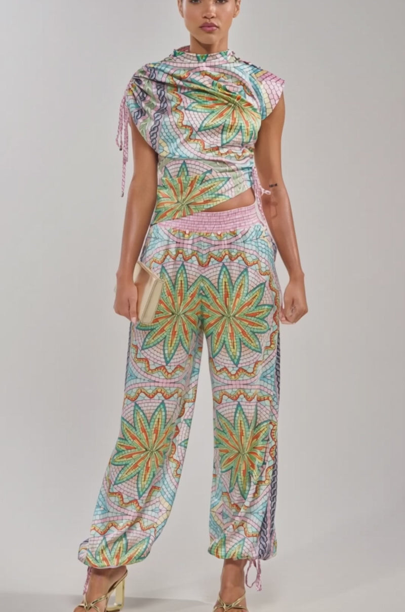 Video of woman modeling the ALL DIFFERENT WAYS SATIN BLOUSE and vibrant pants with starburst designs, holding a small metallic clutch against a plain light background.