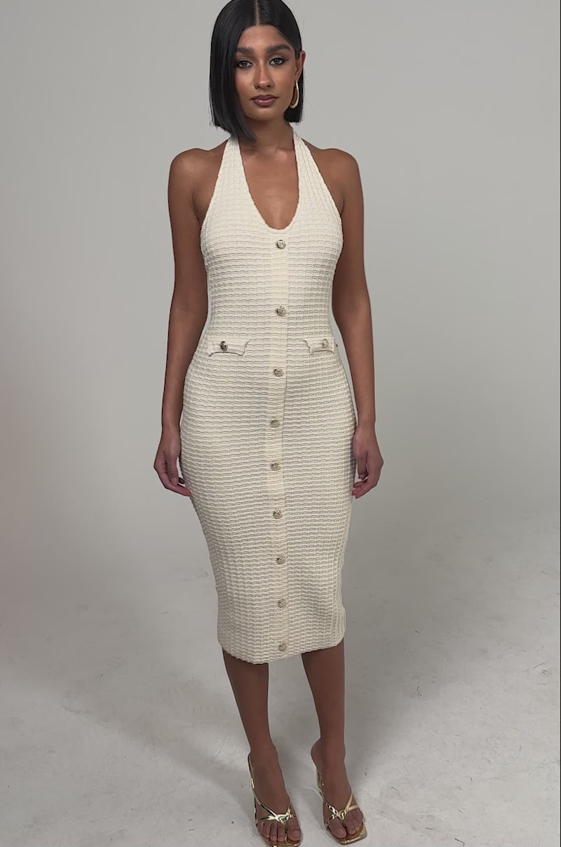 A video of a woman in the BUTTONED DOWN BADDIE MIDI DRESS IN WHITE—a sleeveless knit dress with gold buttons and two small front pockets. 