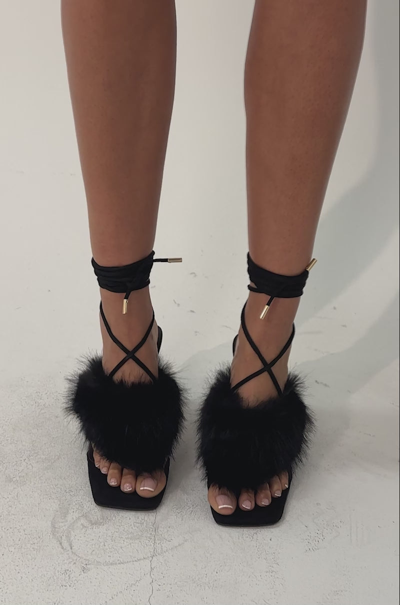 A video of a person wearing the AKIRA GOLD KIRI Black Fur Thong Sandal with a clear heel on a light background.