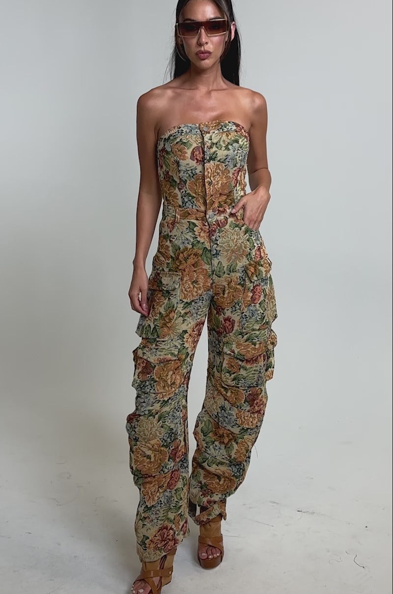 A video of a woman wearing the IN HER ELEMENT FLORAL WOVEN JUMPSUIT IN BROWN MULTI.