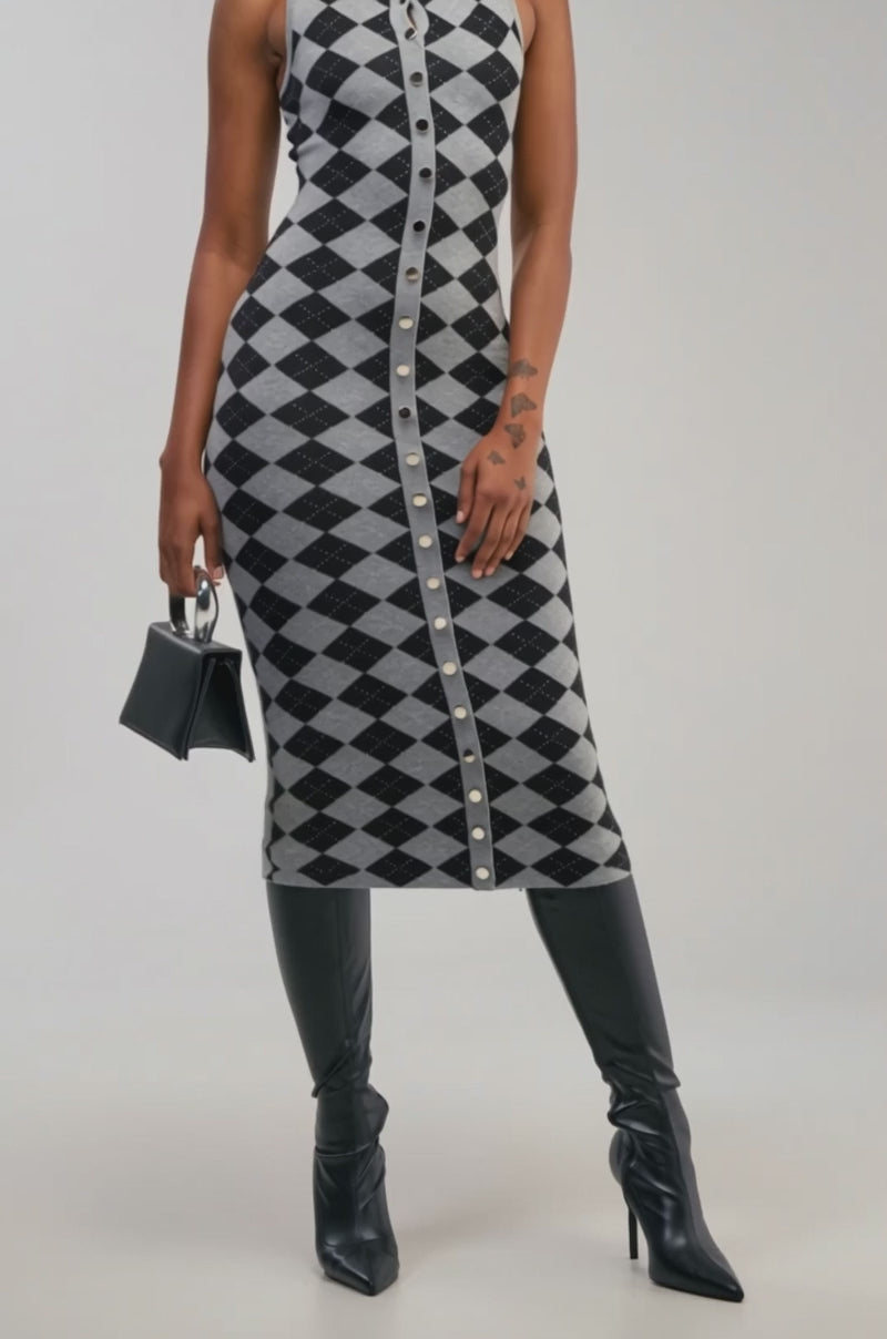 Video of a woman modeling the CLASSY BITCH KNIT ARGYLE SWEATER DRESS—a sleeveless, button-front maxi dress with a gray and black diamond pattern.