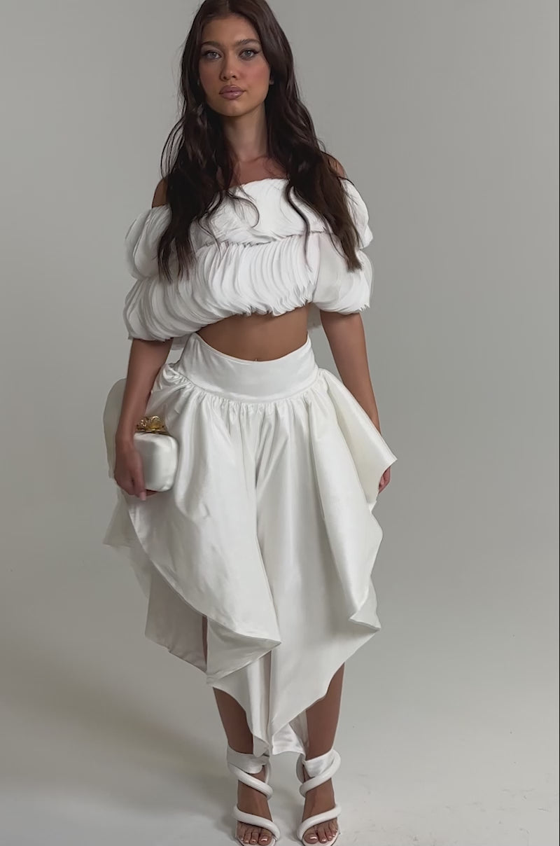 Video of woman modeling the COOL GIRL SKIRT PANT, paired with a white off-shoulder crop top with puffed sleeves and white high-heeled sandals, standing against a plain light background.