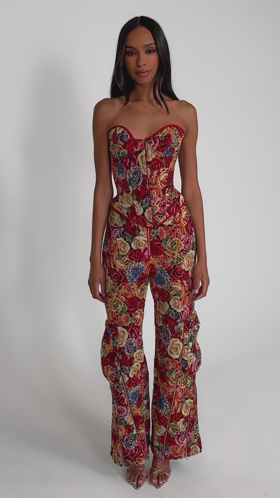 Video of woman modeling the INTO THE THICK OF IT FLORAL BROCADE CORSET, a strapless, vintage-inspired piece with a vibrant multicolored rose pattern and front button detail, set against a plain light background.