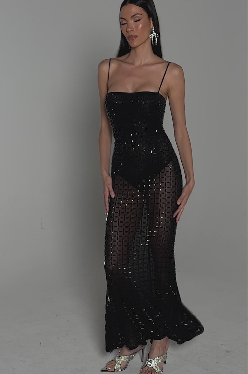Video of woman modeling the UNTOUCHABLE RHINESTONE MAXI DRESS, a fitted, sleeveless black gown featuring thin straps and a textured grid pattern. She holds a small round clutch and strappy heels, posing against a plain, dark background.