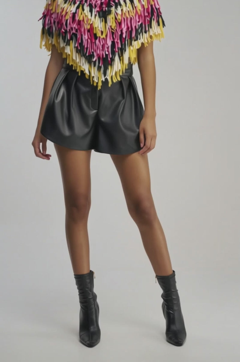 Video of woman modeling the WILD SIDE CROPPED FRINGE PONCHO, which features multicolored fringe in pink, yellow, black, and white, paired with high-waisted black pants against a plain background.