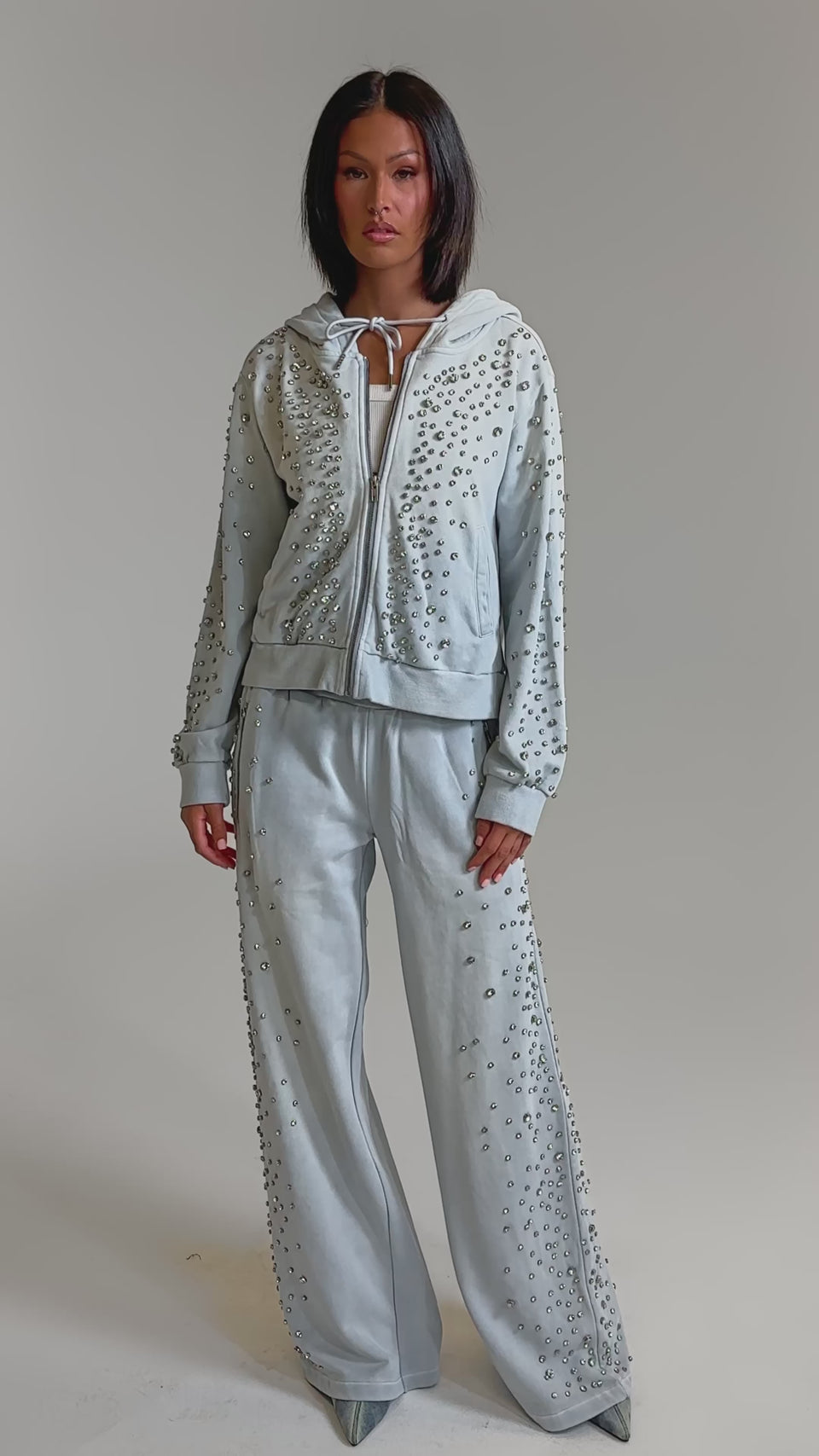 A video of a woman in the OH HOT DAMN EMBELLISHED JOGGER, a light blue rhinestone loungewear set with a matching hoodie and wide-leg sweatpants. 