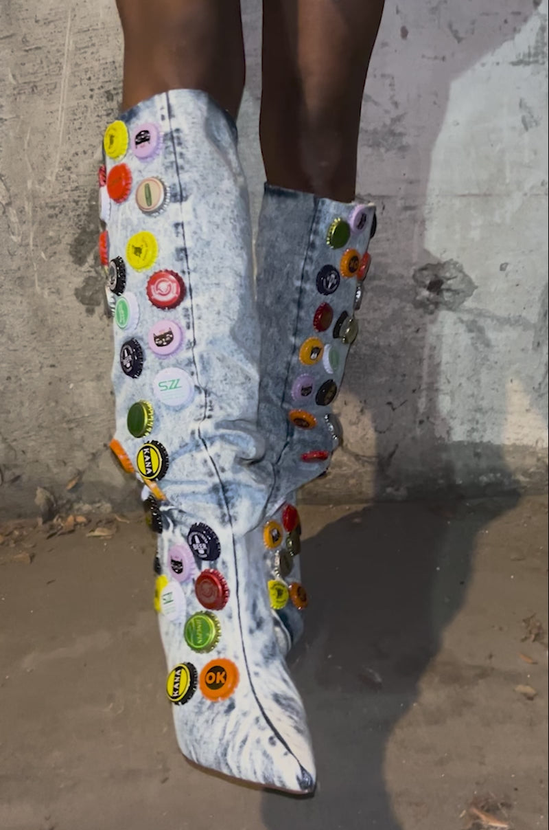 Video of woman modeling the AZALEA WANG THELEN DENIM BOTTLE CAP STILETTO BOOTS, featuring vibrant bottle cap appliqué and a light blue slouchy knee-high design