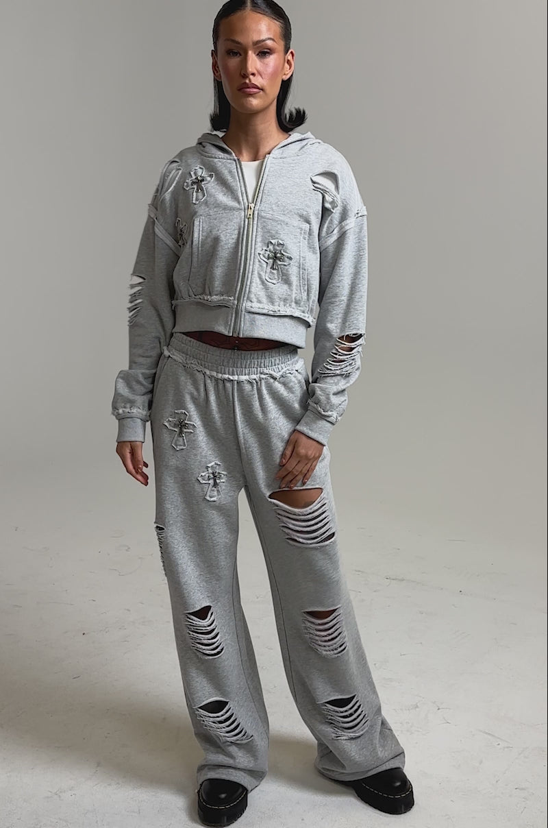 A video of a woman in light gray CROSSED OUT DISTRESSED WIDE LEG JOGGERS with a matching cropped zip hoodie, pairing the look with black platform shoes and sleek, straight hair.