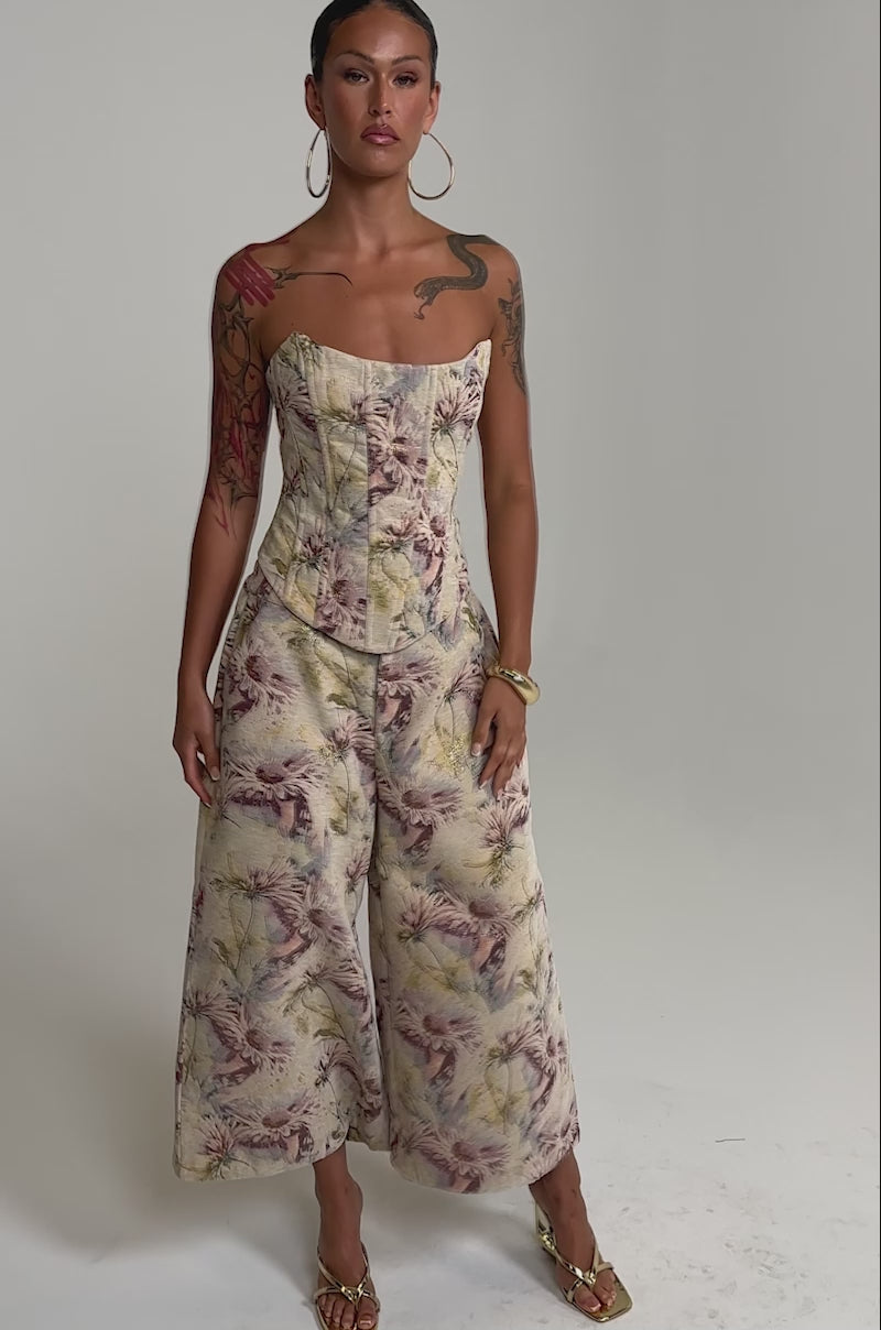 A video of a woman wearing the SWEETIE PIE BROCADE PANT paired with a strapless fitted top, gold hoop earrings, and heeled sandals.