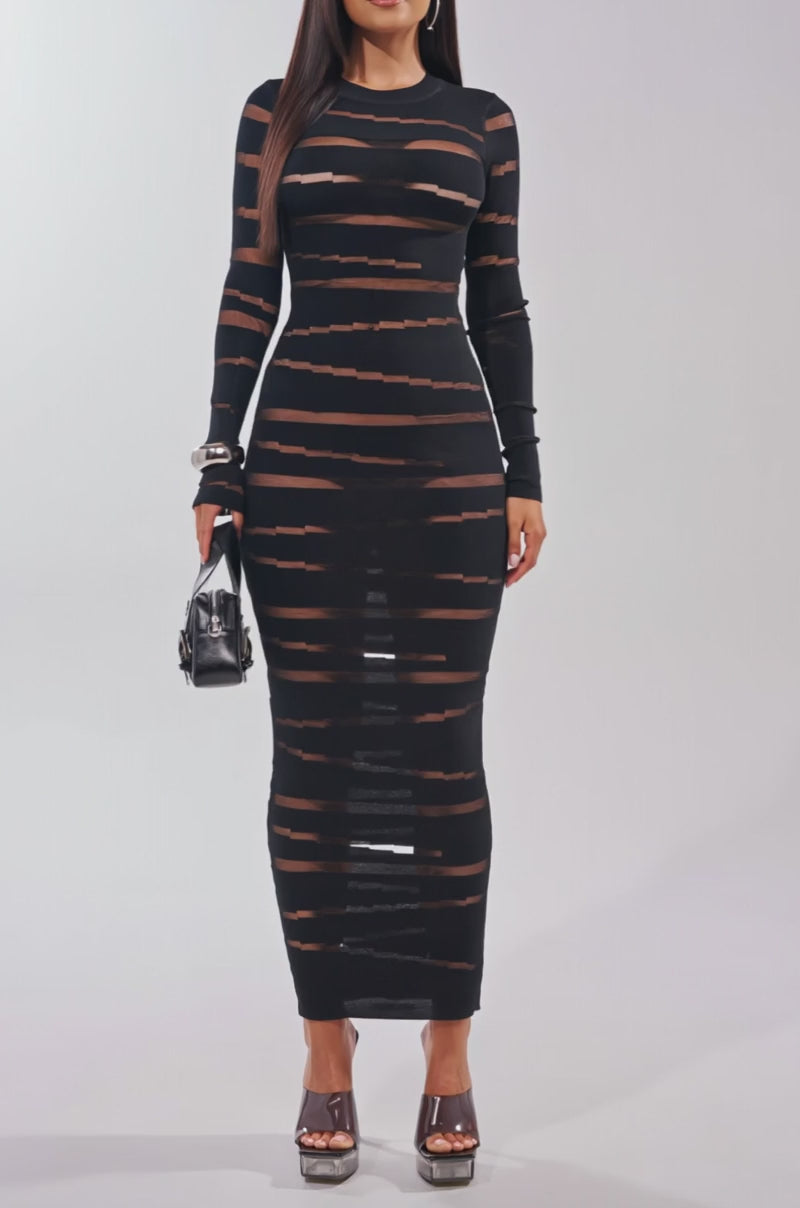 Video of woman modeling the CUT IT OUT LONG SLEEVE KNIT MAXI DRESS—black, sheer mesh panels with horizontal stripes. She accessorizes with sunglasses, heeled sandals, and a small purse against a plain light background.
