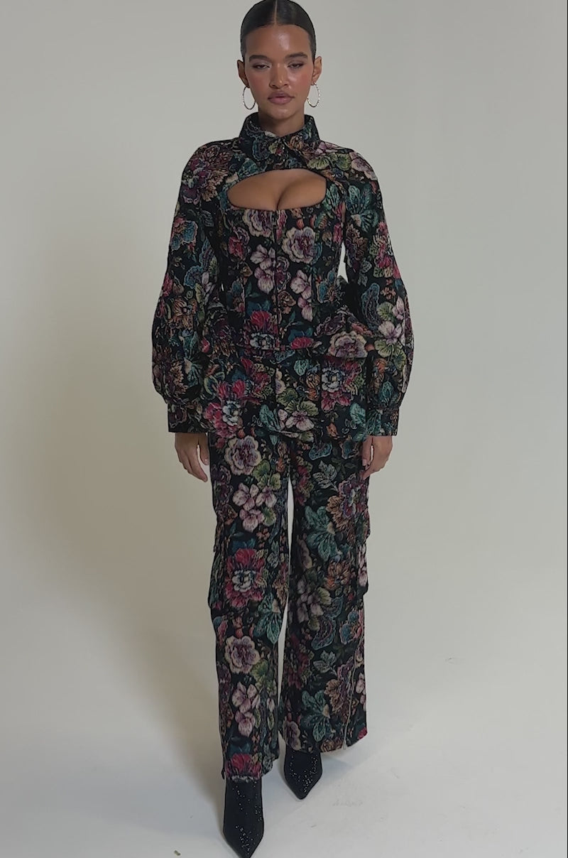 Video of woman modeling the PRETTY LITTLE LADY BROCADE TROUSER—high-rise, wide-leg pants with a colorful floral pattern—paired with black pointed-toe shoes, standing on a white background for a chic, modern look.