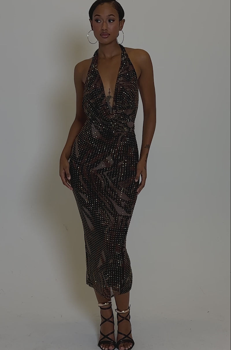 Video of woman modeling the LENNON PRINTED MESH RHINESTONE MIDI DRESS—a sleeveless, dark brown, V-neck gown with sparkling embellishments. She pairs it with black heels and stands against a plain grey background