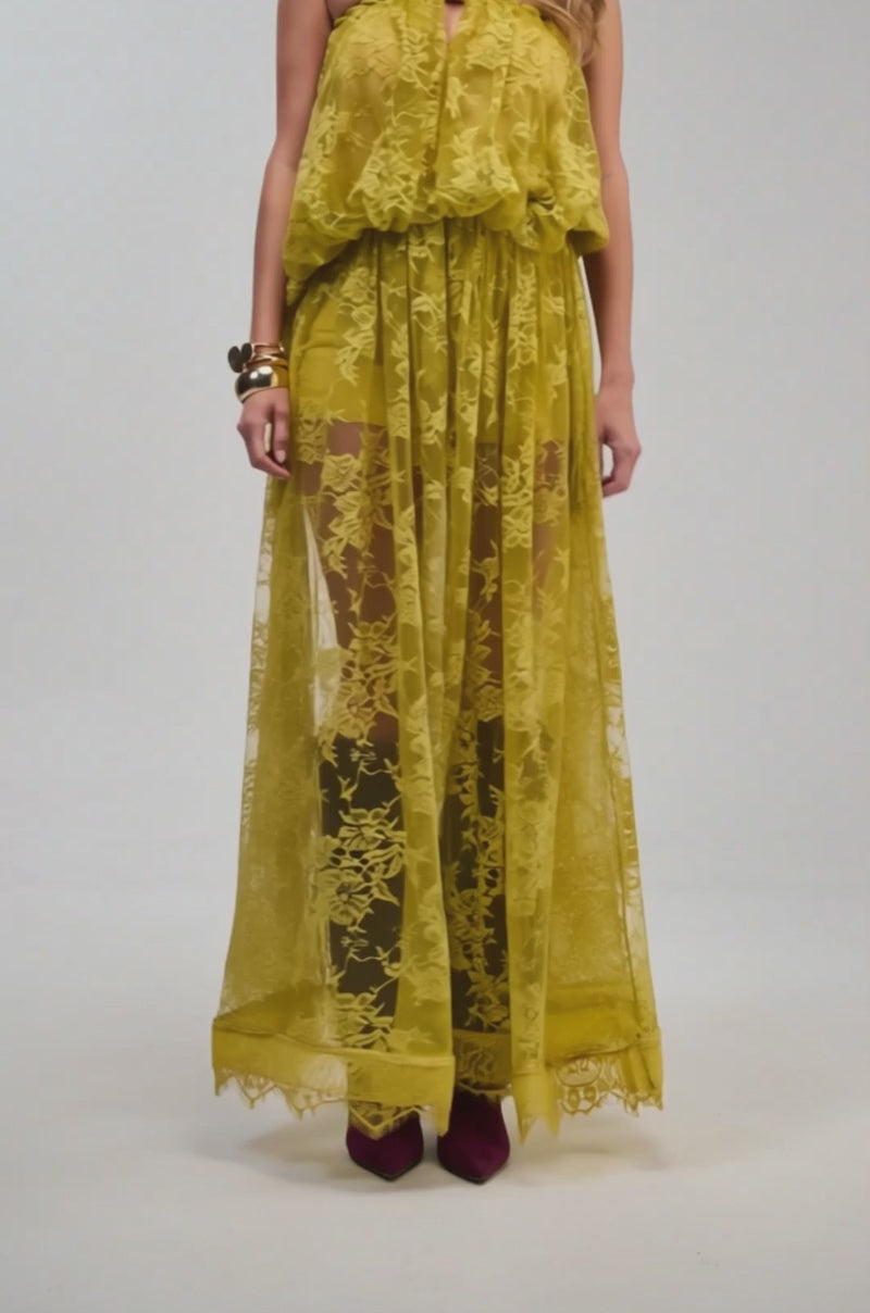 Video of a woman modeling the HANNAH LACE MAXI SKIRT in a sheer yellow lace with a cinched waist and wide-leg silhouette reminiscent of a chartreuse hue. 