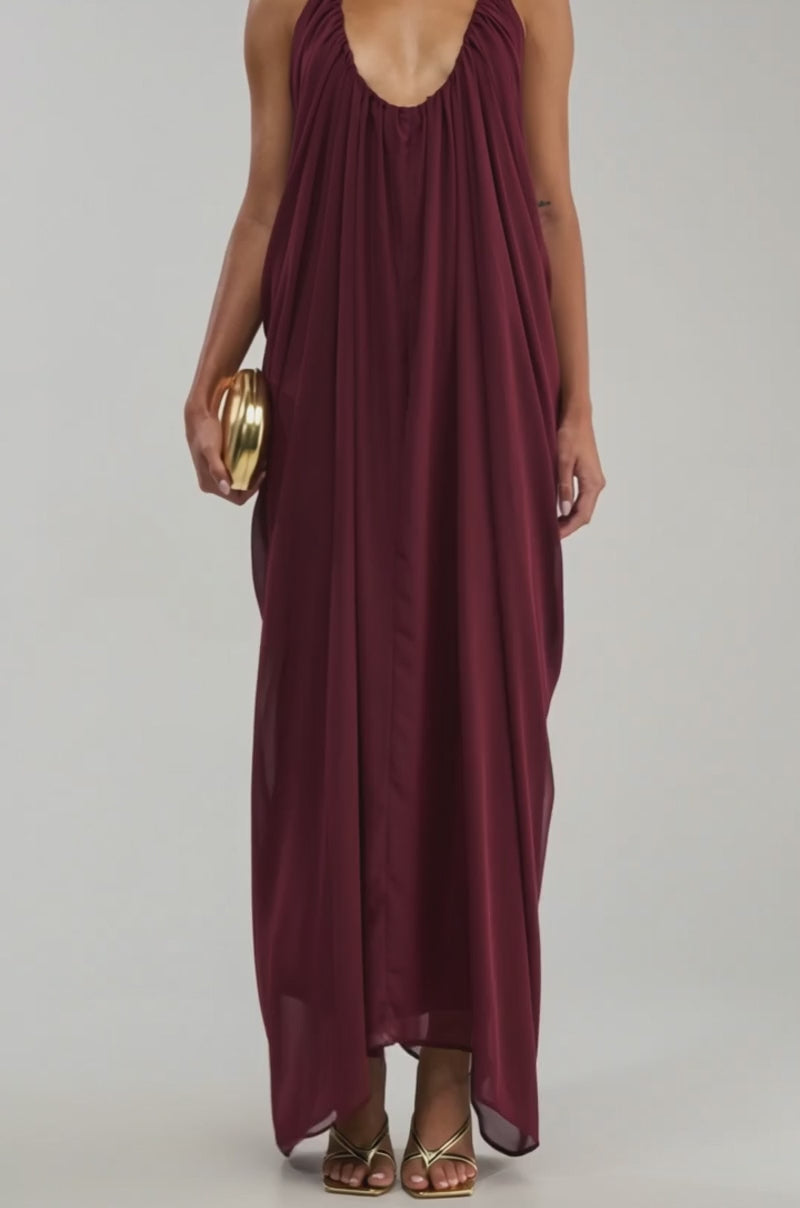 Video of a woman modeling the RAMONA PLEATED MAXI DRESS IN BURGUNDY, styled with gold hoop earrings, gold sandals, and a small gold clutch.