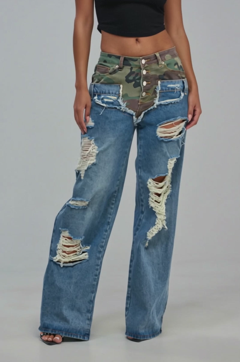 Video of a woman modeling the “ITS GIVING RELAXED DENIM” jeans—medium blue, wide-leg silhouette, featuring a camo-print waist and large distressed holes.