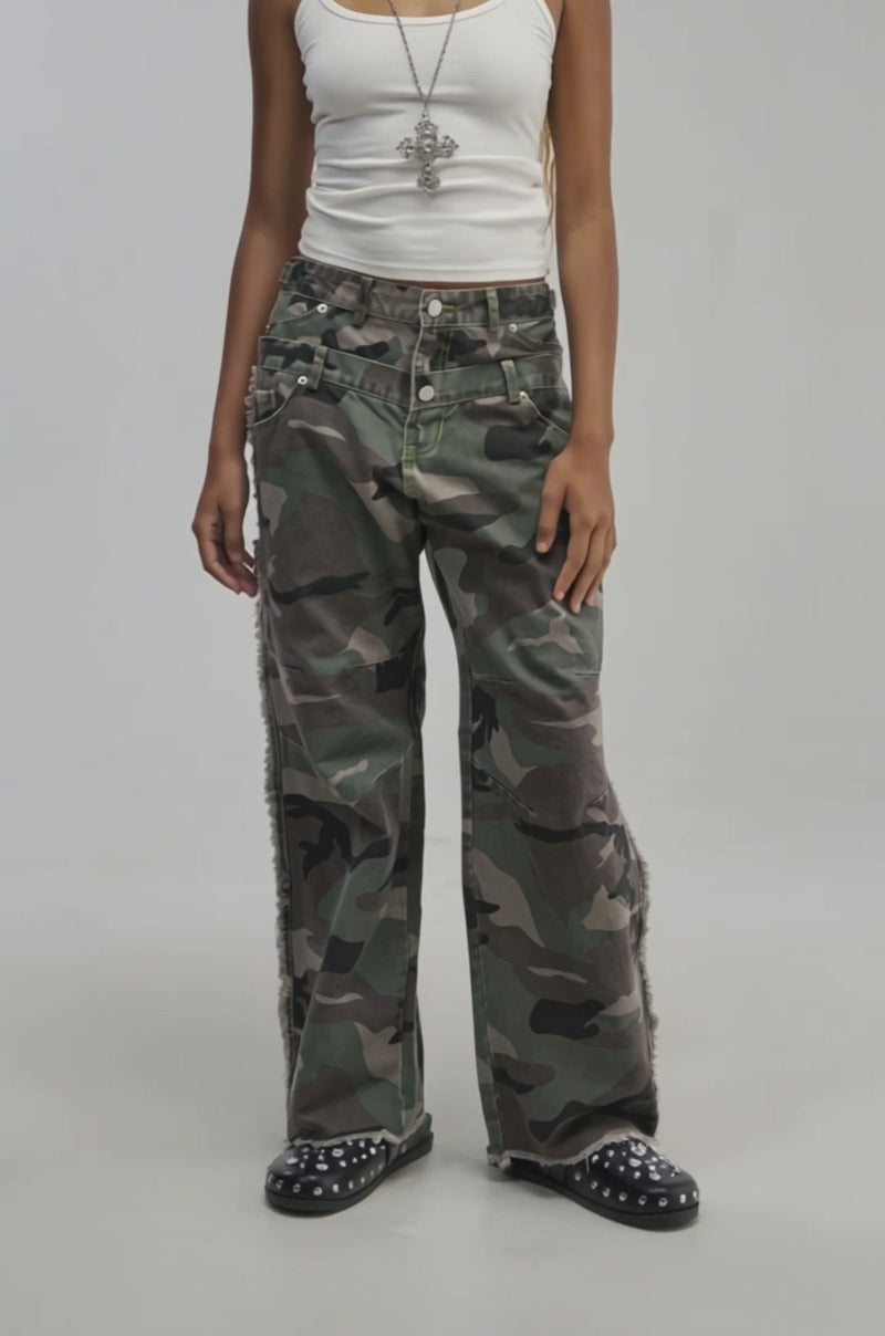 Video of a woman modeling the COOLEST ON THE BLOCK DOUBLE WAISTED CAMO PANT. The camo pants have a loose, wide-leg silhouette with utility details and frayed edges.