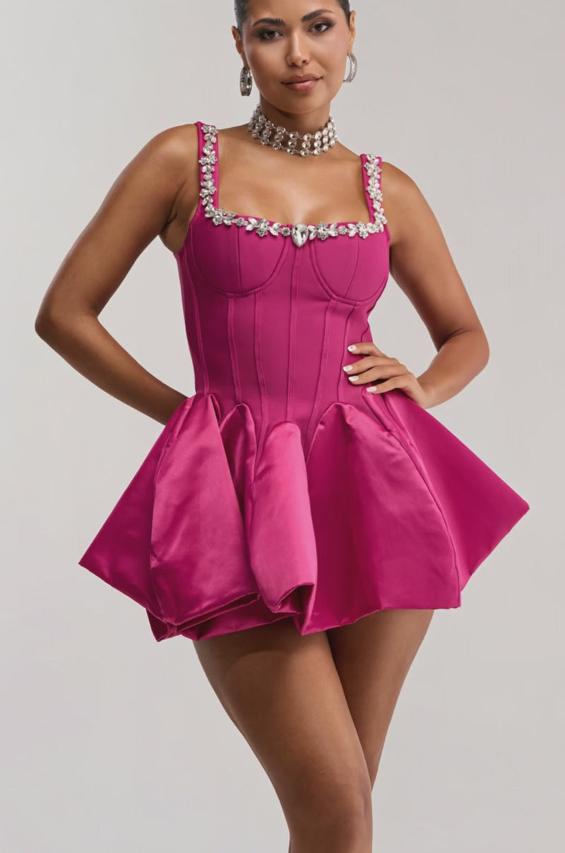 Video of woman modeling the SHIMMER FRAME RHINESTONE MINI DRESS IN PINK—a vibrant fit-and-flare cocktail dress with a jeweled neckline—paired with earrings and a choker, set against a plain background.