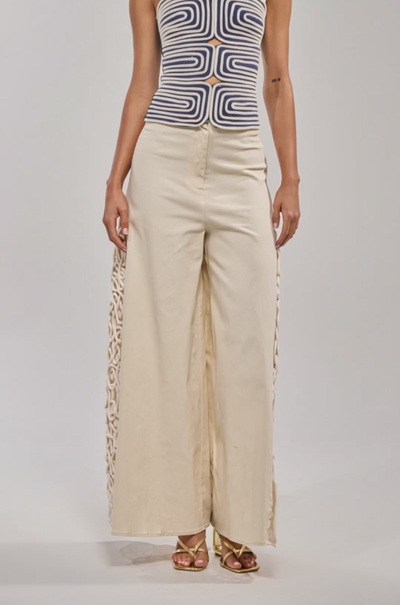 Video of woman modeling the DO NOT DISTURB ROPE TANK, a navy blue and white top with sculptural detail and tied straps, paired with light pants against a plain background.