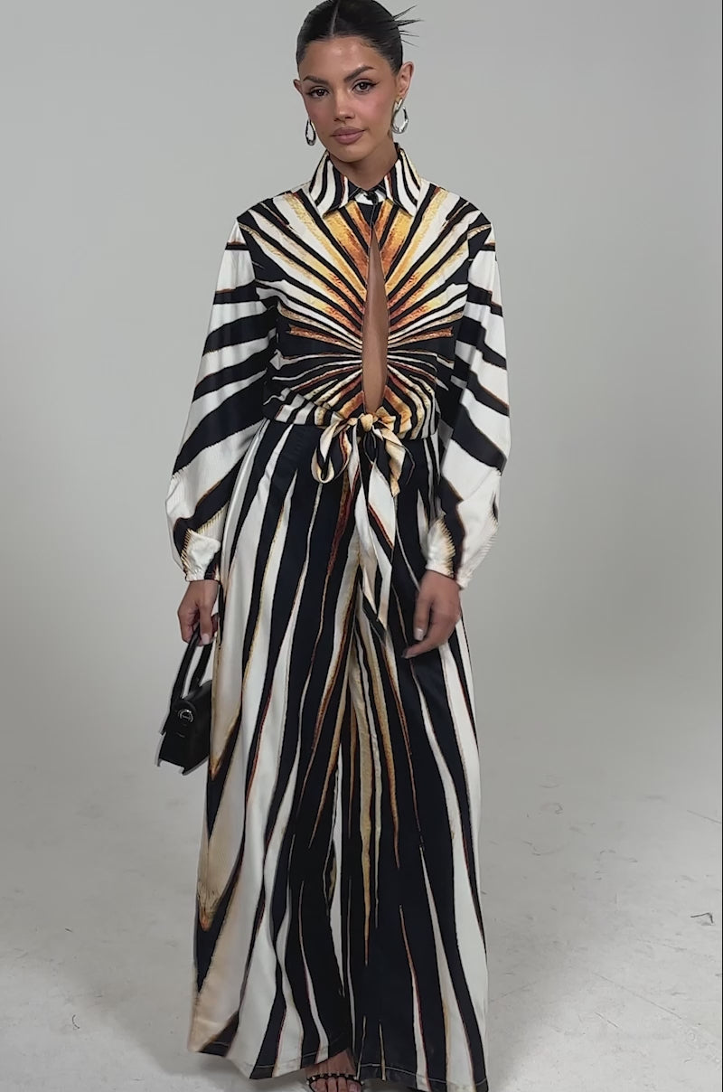 Video of woman modeling the FIERCE INSTINCTS LONG SLEEVE JUMPSUIT featuring a bold tiger print, front keyhole cutout, and waist tie—styled with black heels, a small black purse, and large hoop earrings for a chic vacation dinner look.