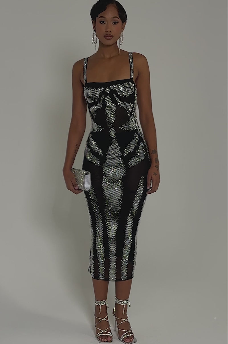 Video of woman modeling the AURA RHINESTONE MESH PRINTED MIDI DRESS, featuring curve-hugging mesh fabric with sparkling silver accents. She accessorizes with a small clutch and strappy heels.