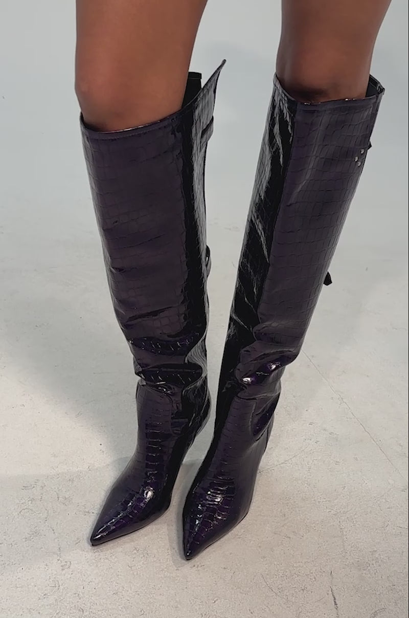 Video of woman modeling the AZALEA WANG GESINE PURPLE CROC PATENT LUXE BOOT with pointed toes and decorative buckles, standing against a plain background.