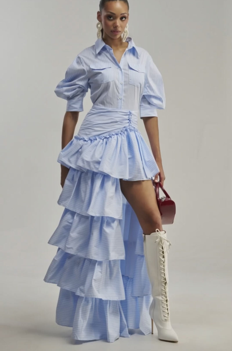 Video of a woman modeling the IT’S A DATE POPLIN MAXI DRESS IN BLUE, featuring ruffled details and a high-low hem.