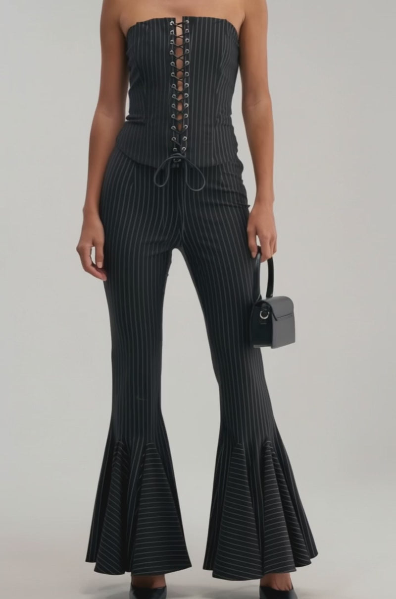 A video of a woman wearing LIVI STRETCHY PINSTRIPE FLARE LEGGINGS, paired with a strapless black top, black heels, and holding a small black handbag. 