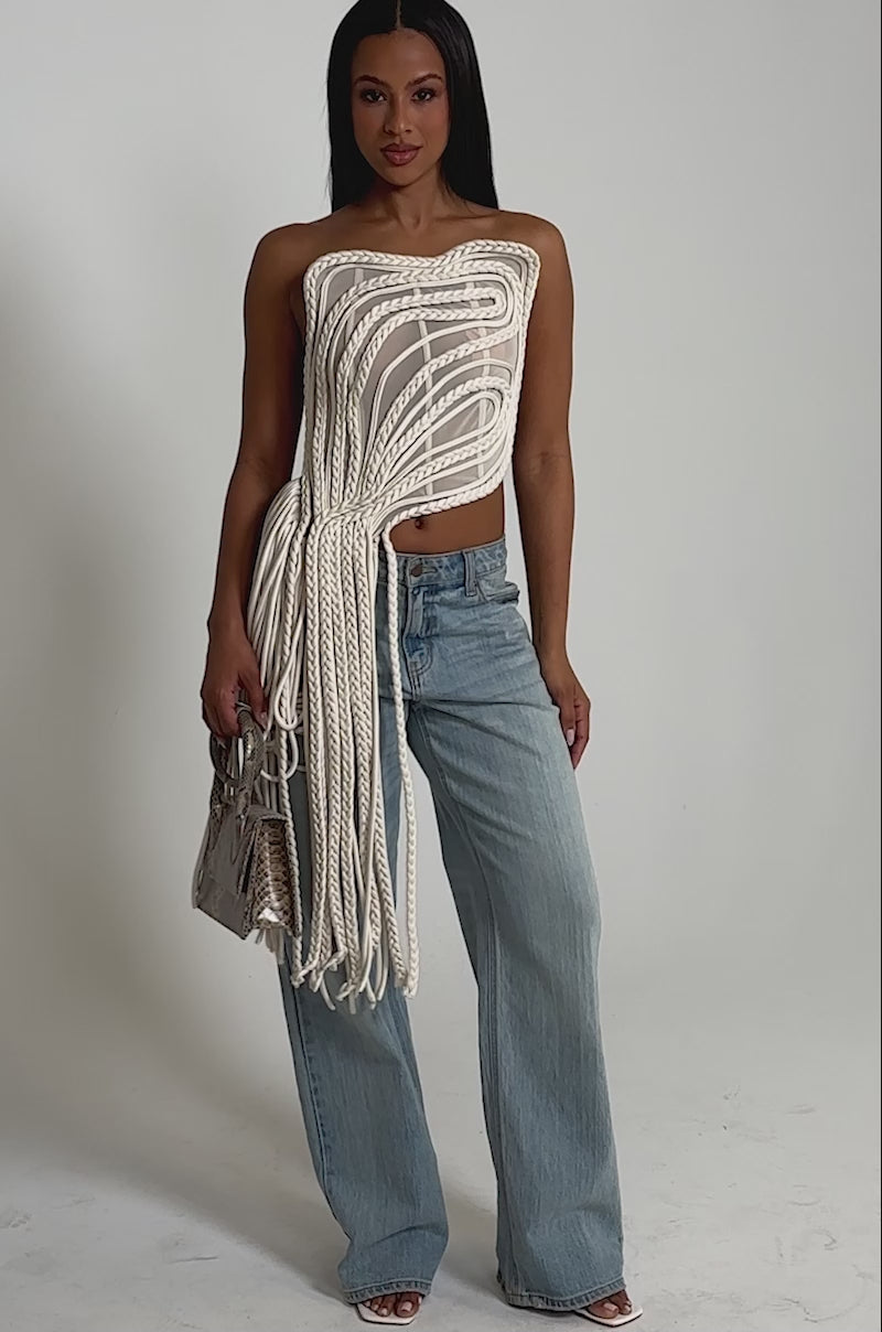 A video of a woman wearing the CUTTING YOU OFF MESH ROPE CORSET, light blue wide-leg jeans, heels, and holding a small handbag.