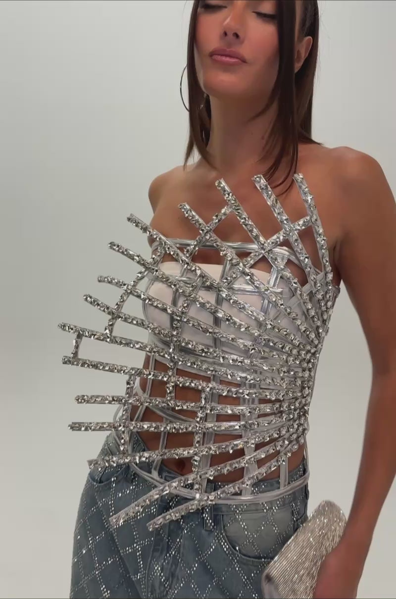 A video of a woman in the MADE YA LOOK RHINESTONE CAGE CORSET and loose, diamond-patterned blue jeans holding a sparkly clutch. 