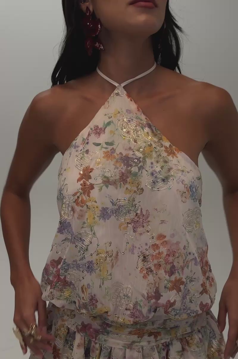 Video of a woman modeling the GARDEN PARTY MINI DRESS IN WHITE FLORAL—a sleeveless halter mini dress featuring a floral print and a ruffled skirt. 