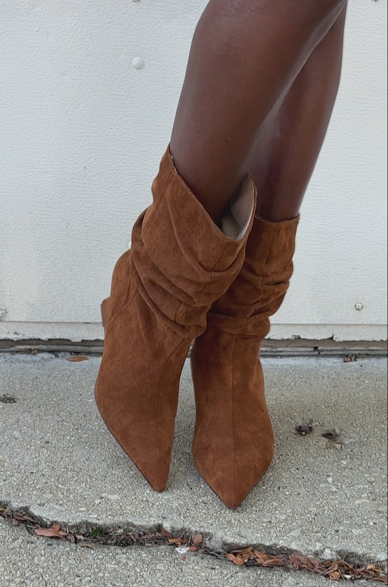 A close-up video of a person wearing the AZALEA WANG ASAF Ruched Wedge Bootie in tan, featuring a pointed toe and slouchy suede style, standing on concrete near a white wall.