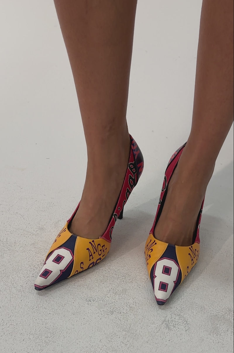Video of woman modeling the AZALEA WANG MULTI PRINTED STILETTO POINTED TOE PUMPS with patchwork graphic designs and numbers, standing on a light background.