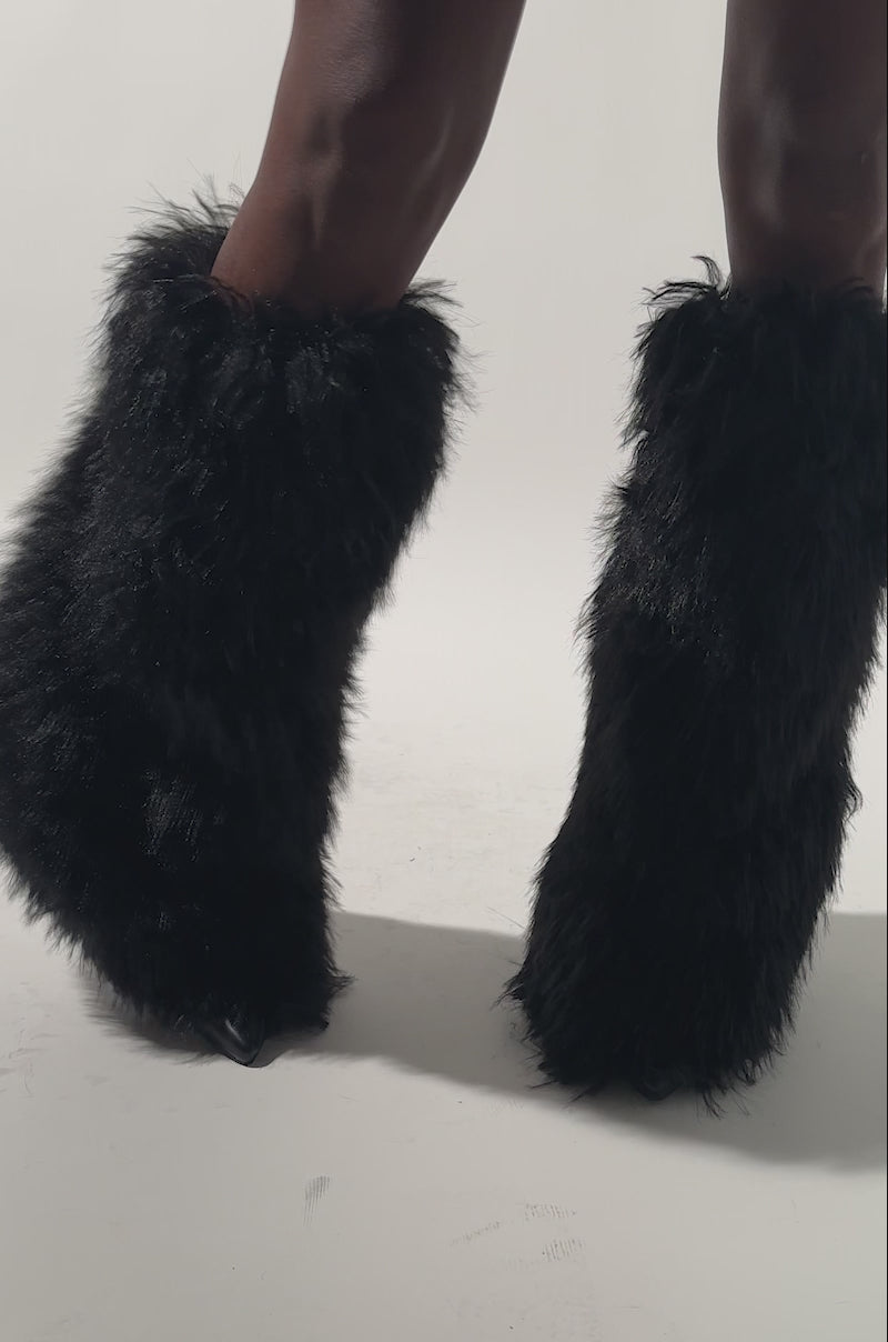 A video of a model standing against a plain background, legs shown, wearing the AZALEA WANG ARETE BLACK FUR STILETTO BOOT paired with a matching black furry skirt.