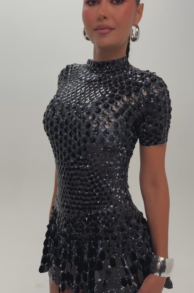 Video of a woman modeling the FAR FROM BASIC SEQUIN MINI DRESS IN BLACK, featuring a short, shiny black design with metallic disc details.