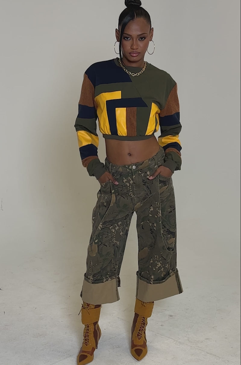 Video of woman modeling the DORA COLOR BLOCKED CROP SWEATSHIRT in olive, yellow, navy, and brown, paired with corduroy camo-pattern pants and gold hoop earrings, standing against a plain background.